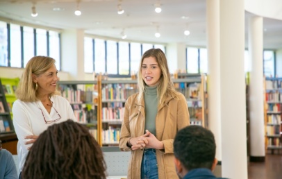 A woman listening to another woman while standing in a library